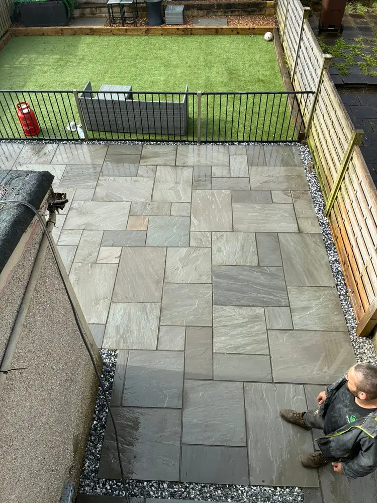 Exterior patio paving project with sandstone slabs and artificial turf area